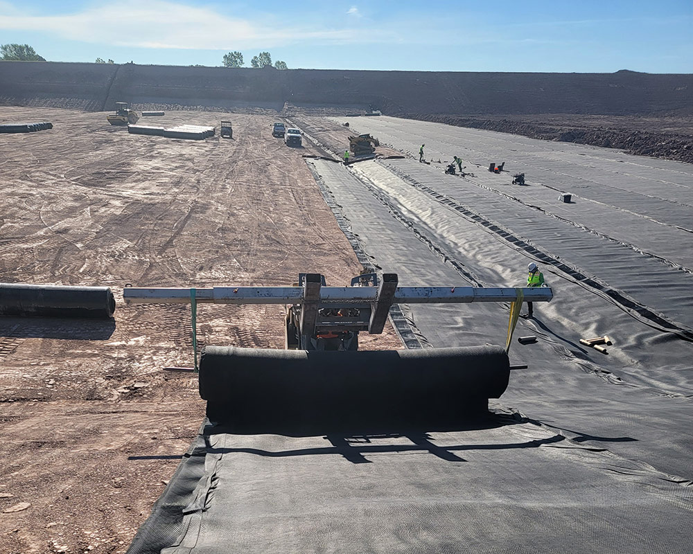 Heavy Equipment Deploying Geomembrane by Utilizing a Spreader Bar