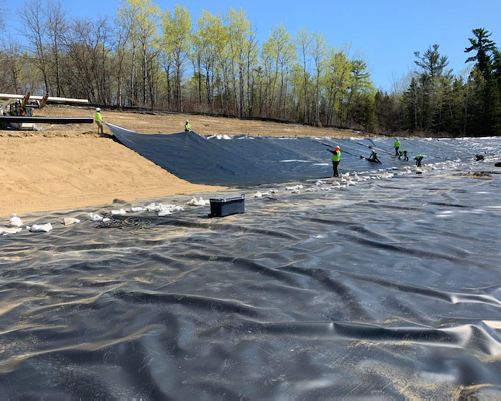 Crews Onsite Installing Geomembrane on the Slope of a Storage Pond